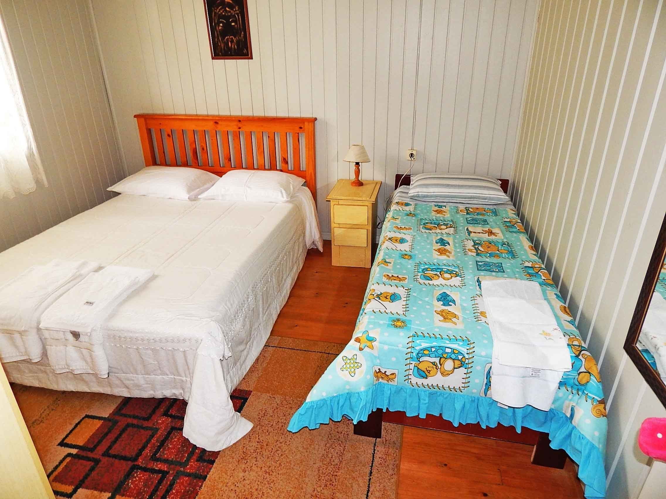 A bedroom with two beds, one with a wooden headboard and the other with a colorful bedspread. There is a nightstand with a lamp and a small table with a lamp.