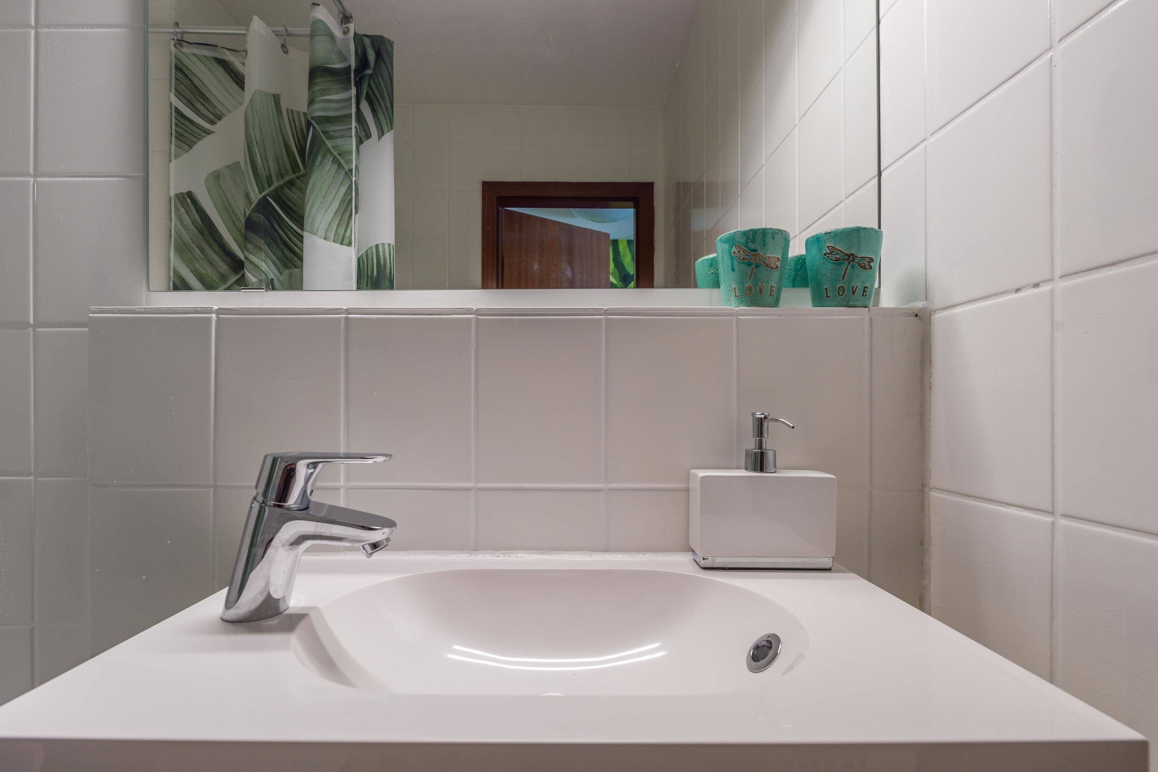 A bathroom with a white sink, chrome faucet, and a small white soap dispenser.