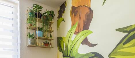 Una habitación con dos sillones de cuero marrón, piso de madera, un radiador, una ventana con persianas y una pared con un gran mural de hojas tropicales.