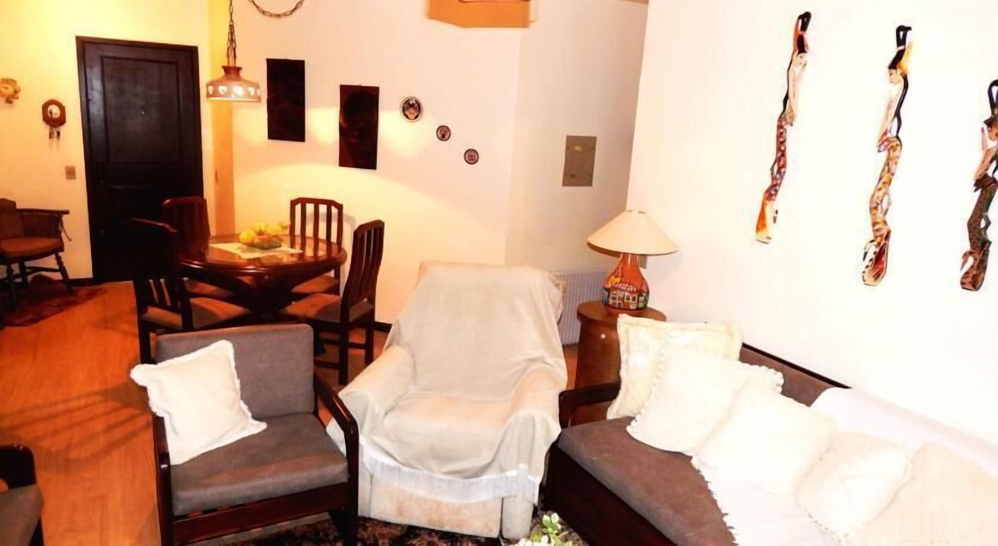 A living room with a sofa, armchairs, a dining table with chairs, a lamp, and wall decorations.