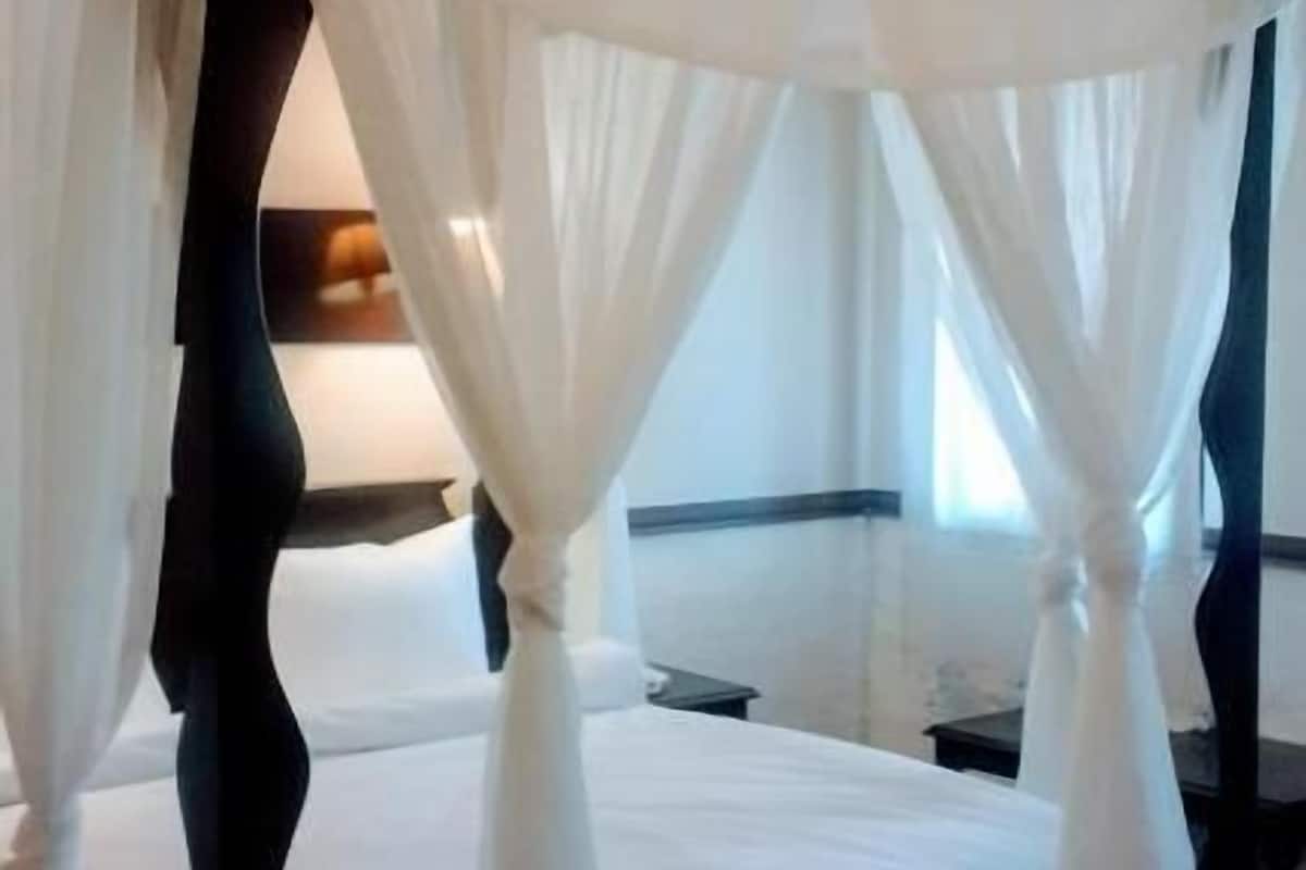Uma cama de dossel com roupa de cama branca e cortinas leves.