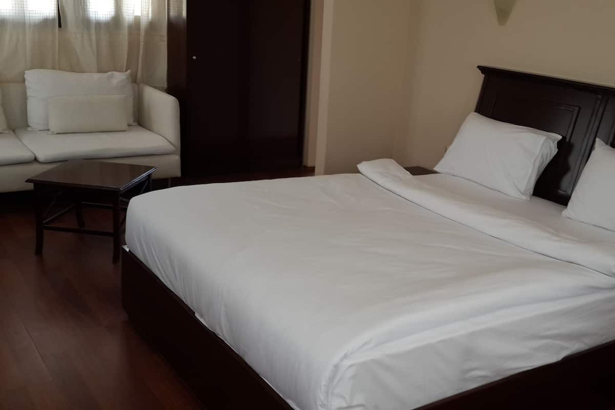 Cama bem arrumada com roupa de cama branca, cabeceira de madeira e uma pequena mesa de madeira ao lado.