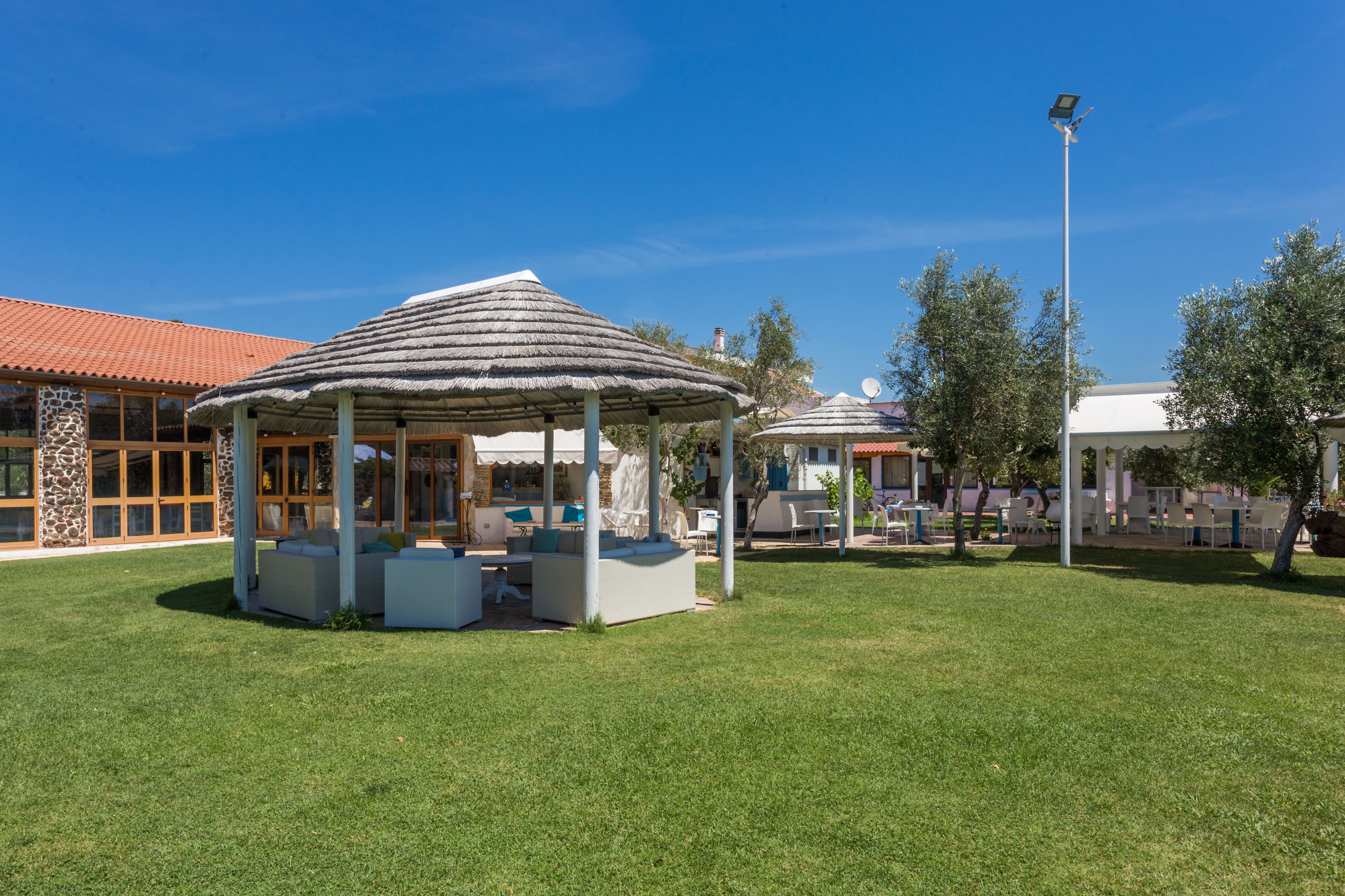 A gazebo with seating, a stone building with large windows, and a clear blue sky.