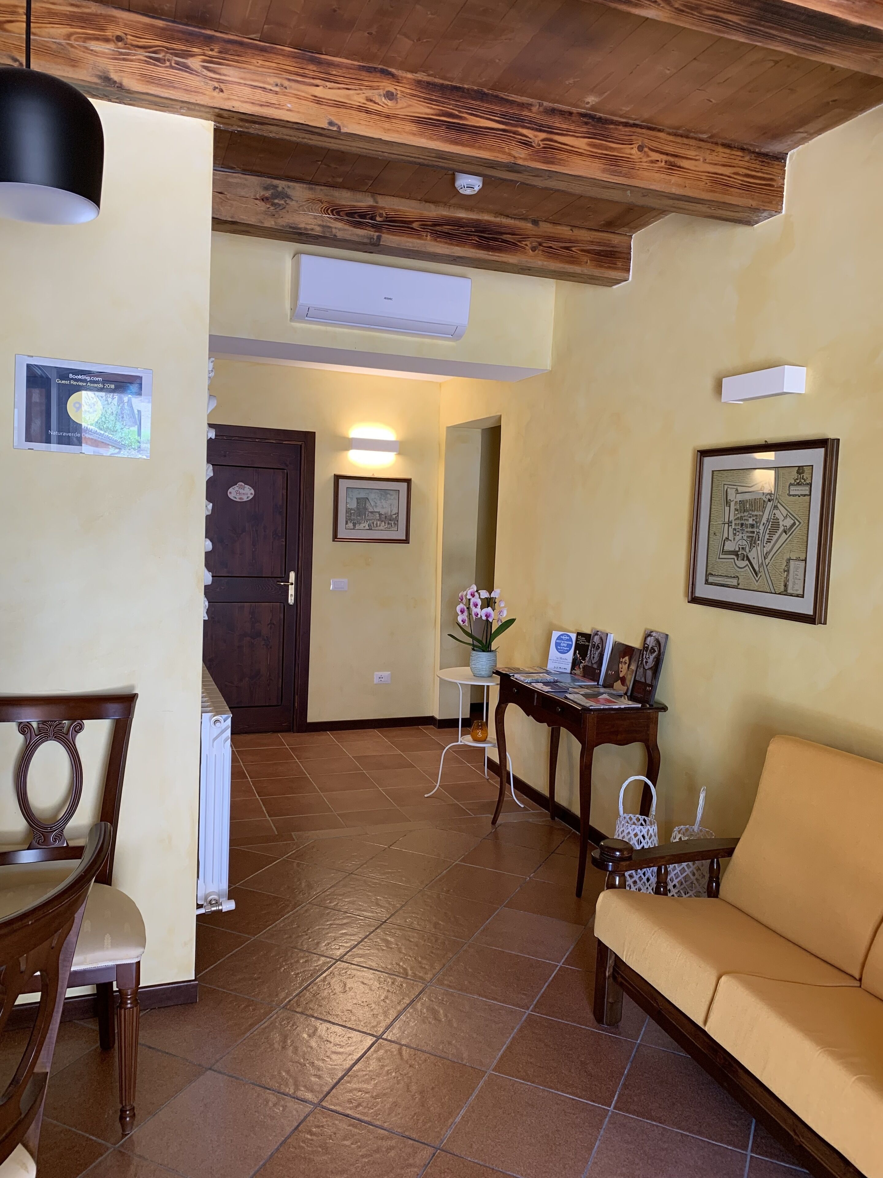 A spacious living area with a wooden ceiling, a dining table with chairs, a sofa, and a small side table with a vase of flowers.
