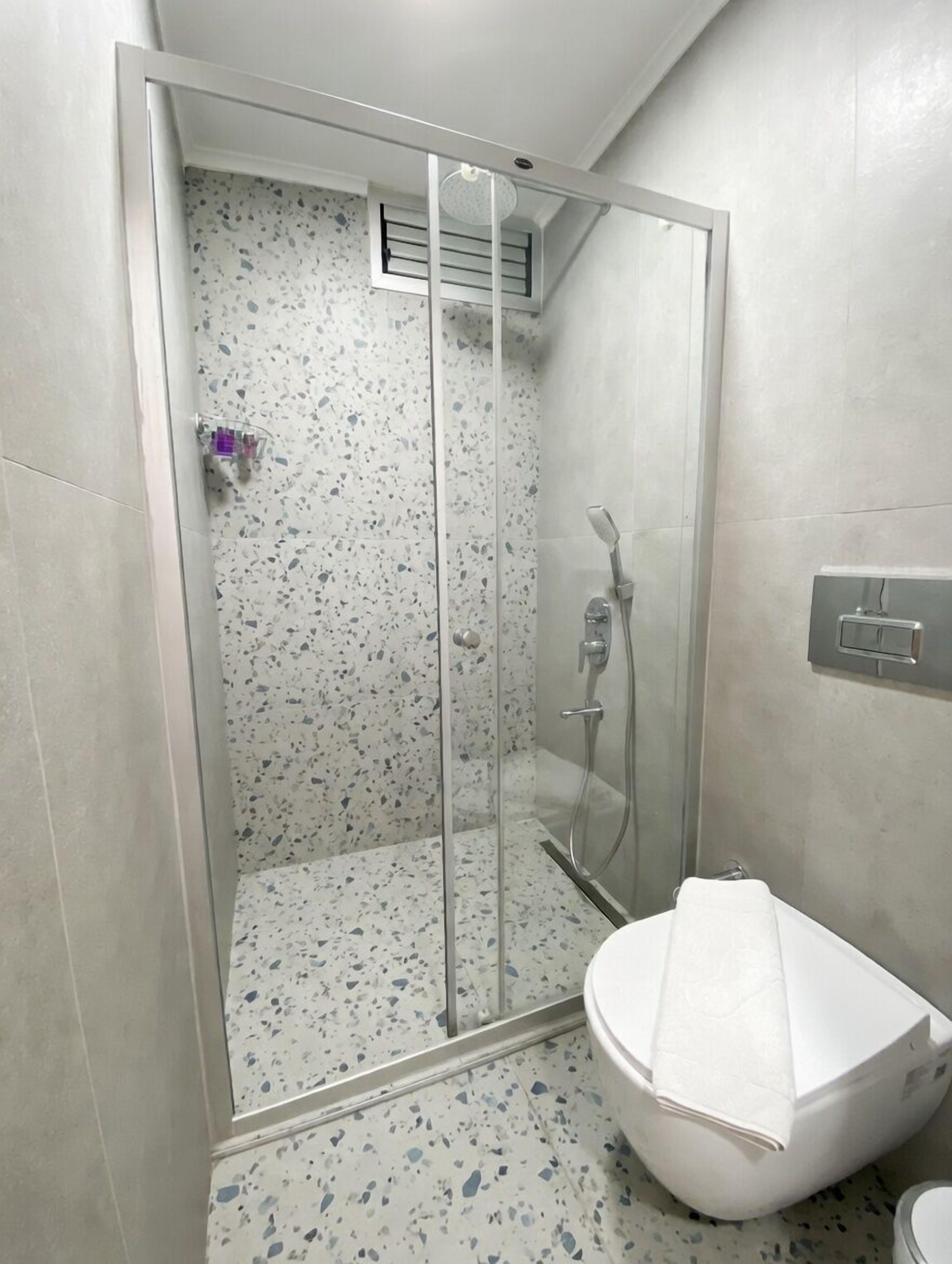 Ducha con puerta de vidrio, inodoro y pulsador de luz en la pared.
