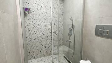 Ducha con puerta de vidrio, inodoro y pulsador de luz en la pared.