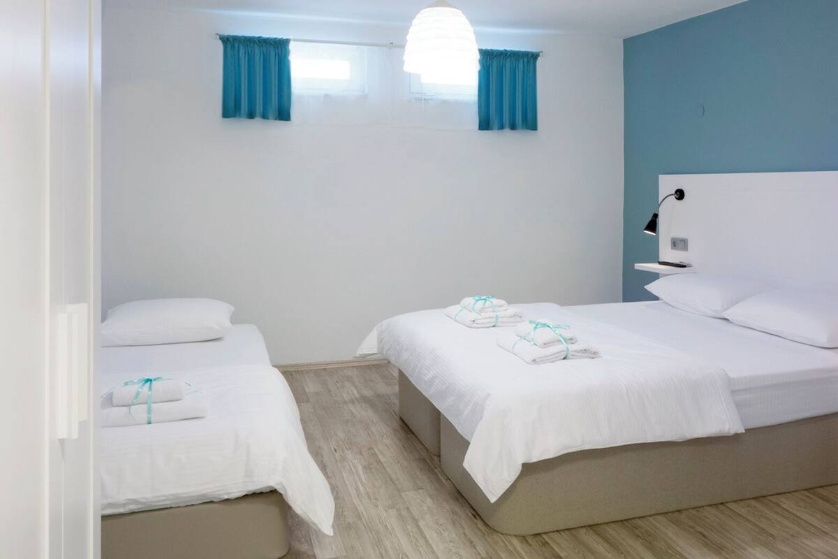 Ein Hotelzimmer mit zwei Einzelbetten, einem großen Bett, einem Nachttisch mit Lampe und einem Fenster mit Vorhängen.