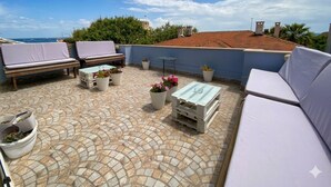 A rooftop terrace with seating, potted plants, and a view of the sea.