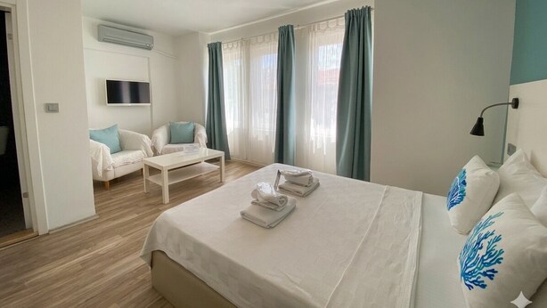 A hotel room with a bed, a sofa, a TV, and a window with curtains.