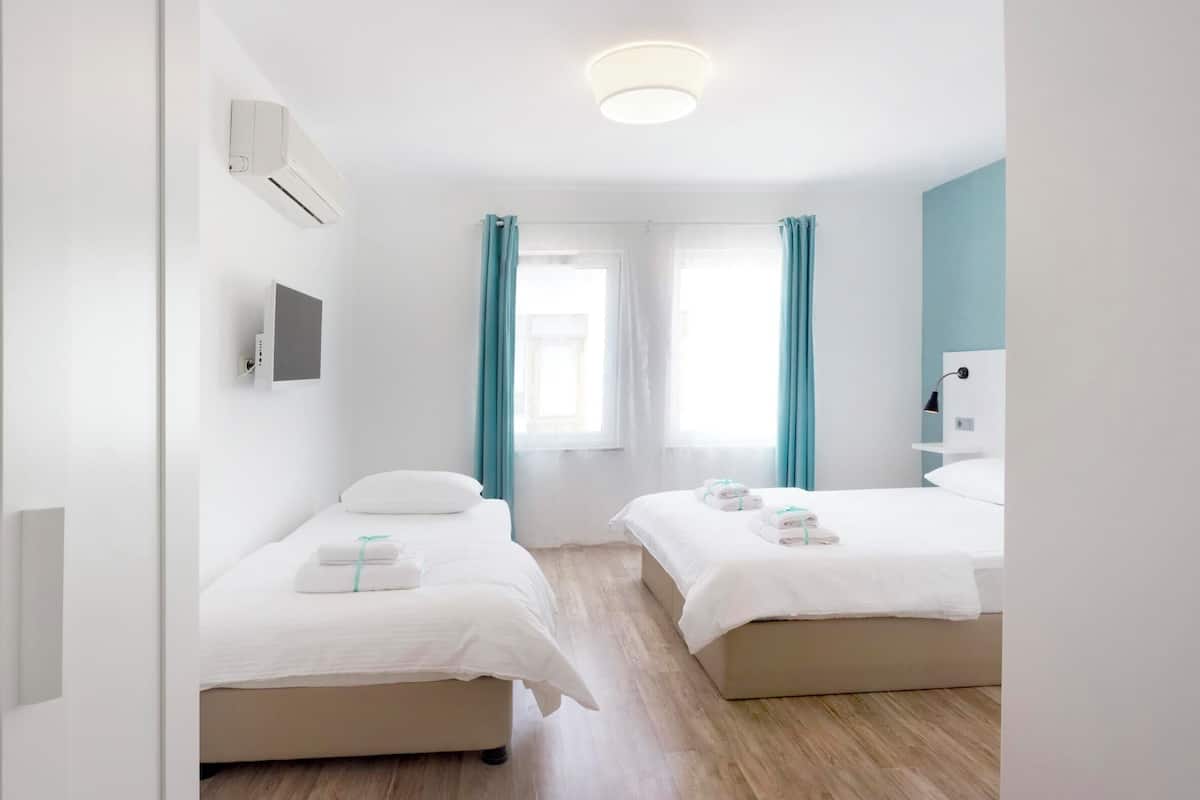 Ein modernes Hotelzimmer mit zwei Betten, einem Flachbildfernseher und einer Deckenleuchte.