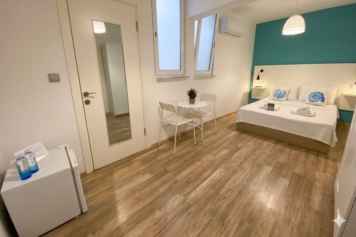Ein Schlafzimmer mit einem Bett, einem Nachttisch, einem Sessel, einem kleinen Tisch und einem Fenster.