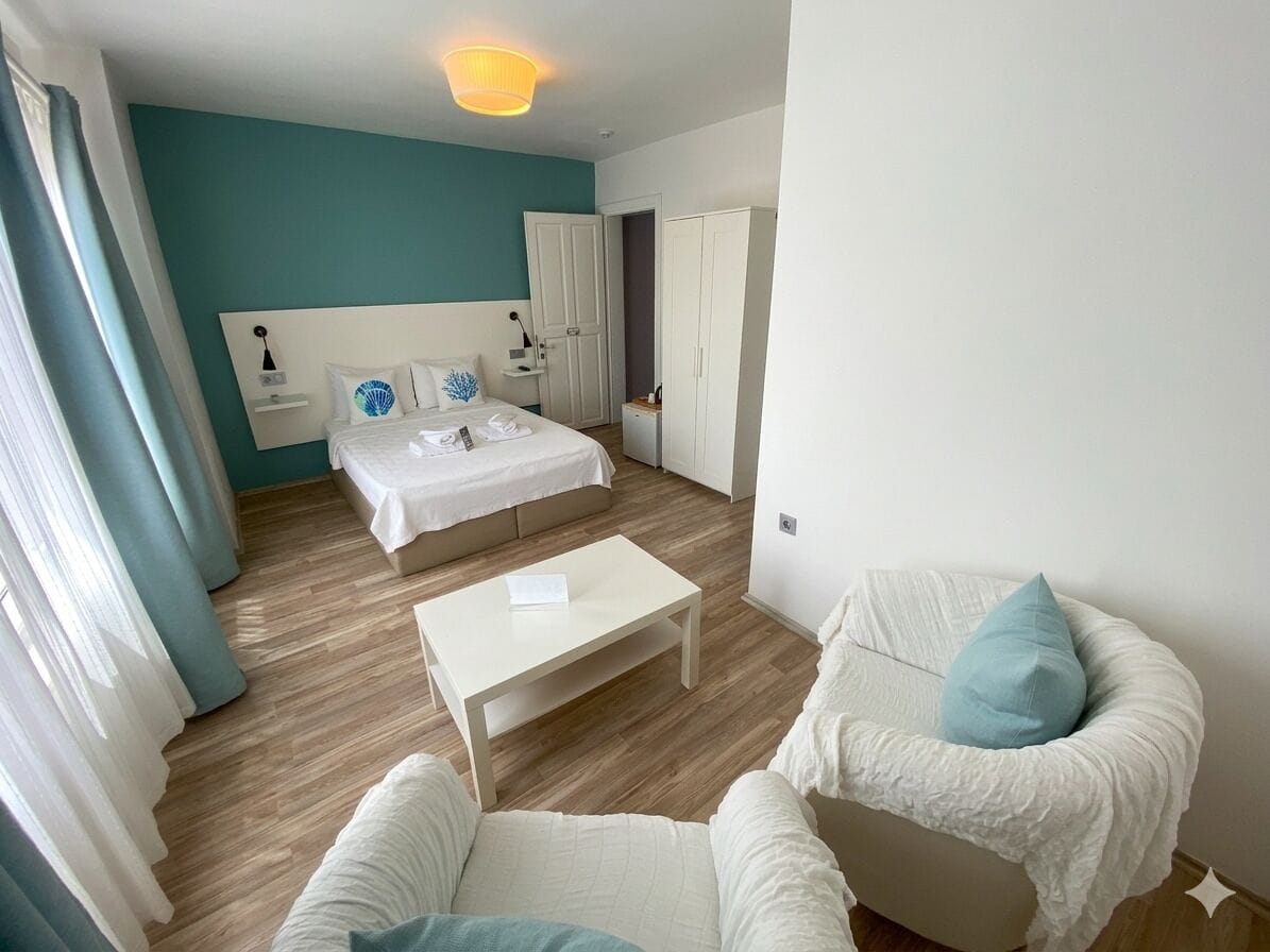 Quarto de hotel moderno com uma cama, uma poltrona branca, uma mesinha e um guarda-roupa.