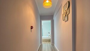 A hallway with patterned flooring, a hanging light fixture, and a door leading to a room.