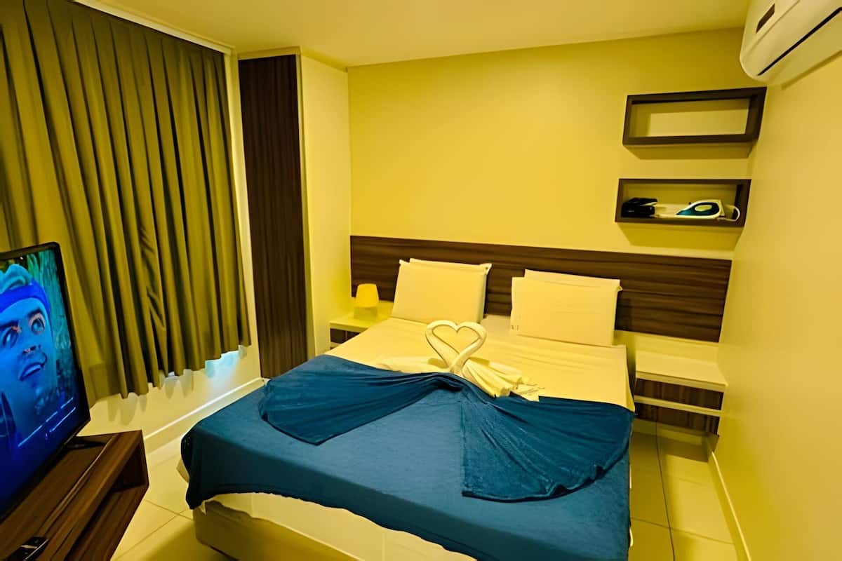 Une chambre d’hôtel équipée d’un lit, d’une télévision, d’une table de chevet et d’une étagère fixée au mur.
