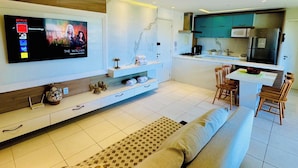 Una sala de estar moderna con una televisión de pantalla plana, un sofá, una mesa de centro y una zona de cocina con refrigerador y microondas.