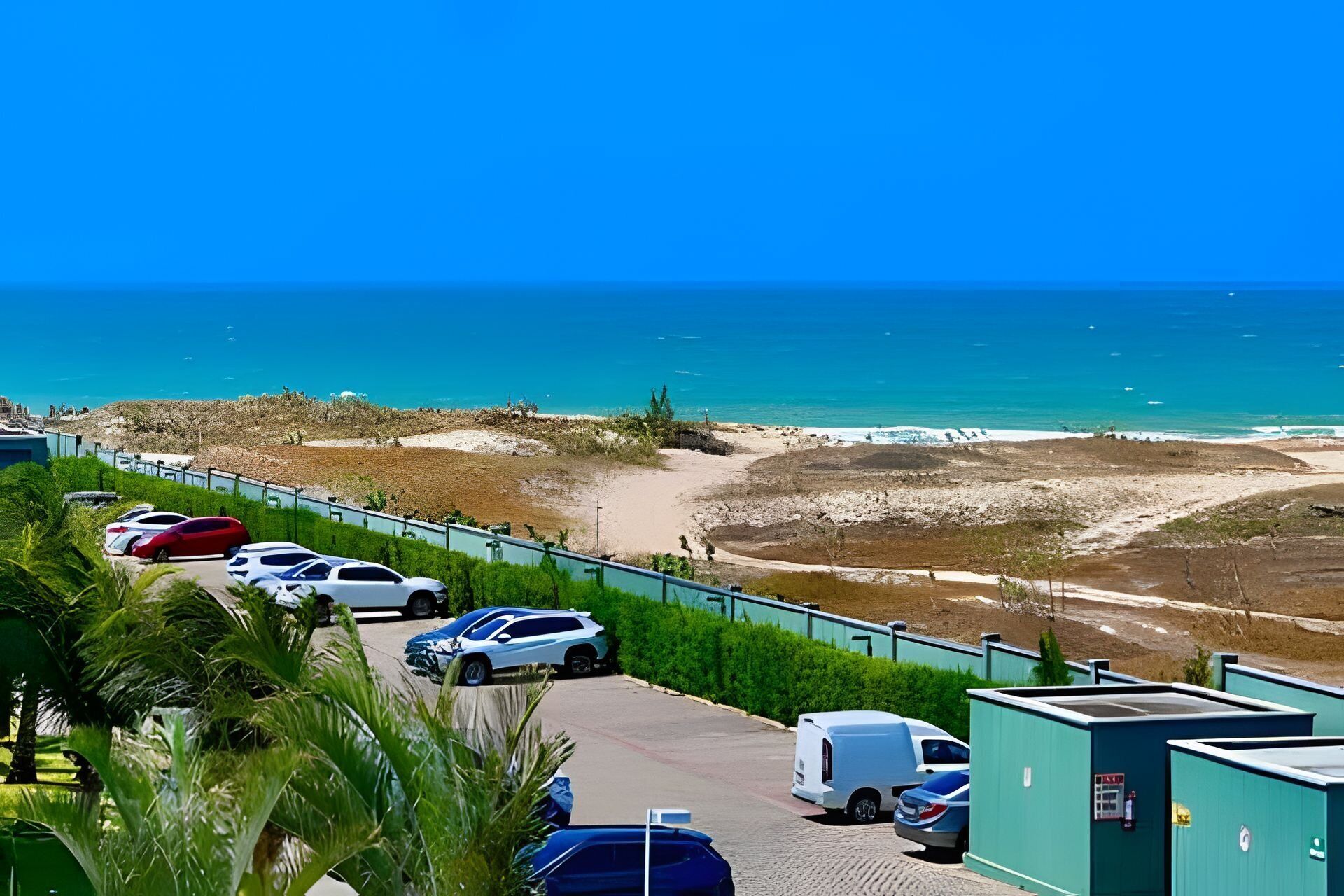 A parking area with vehicles, a pathway, and a view of the beach and ocean.