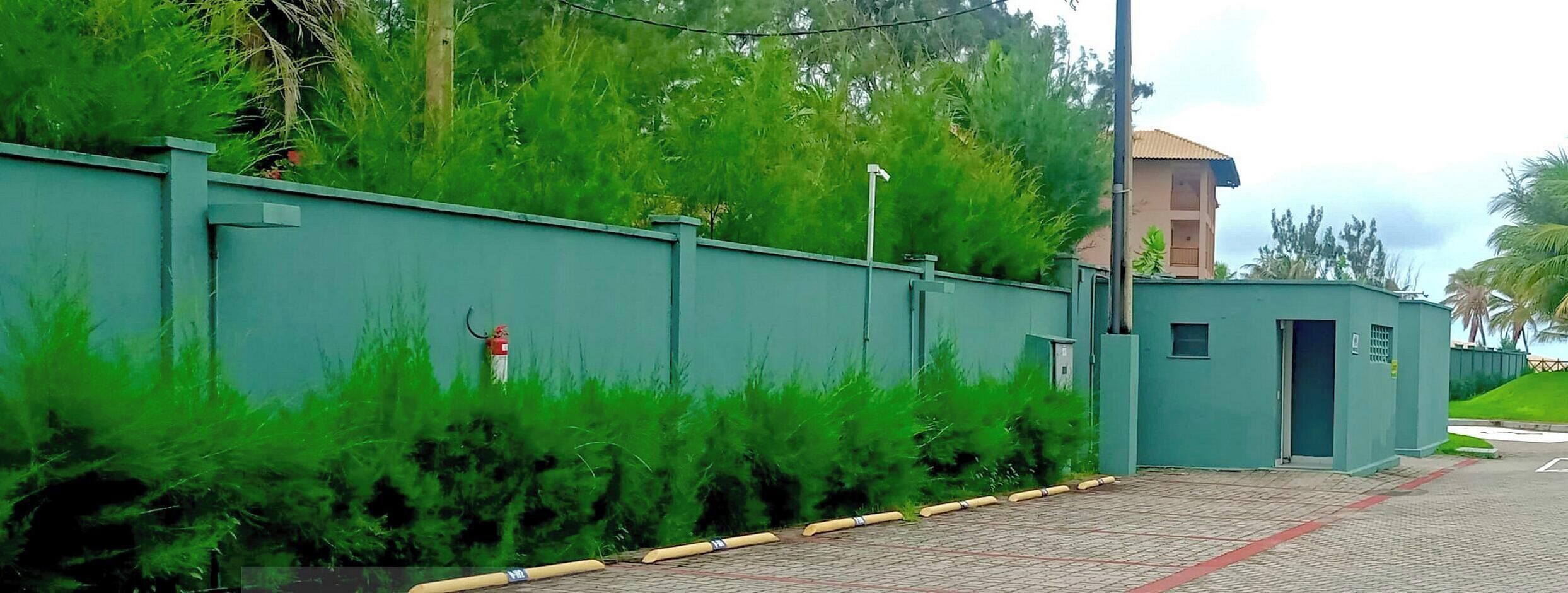 Un'area recintata con un muro verde, un estintore e un edificio con tetto marrone sullo sfondo.