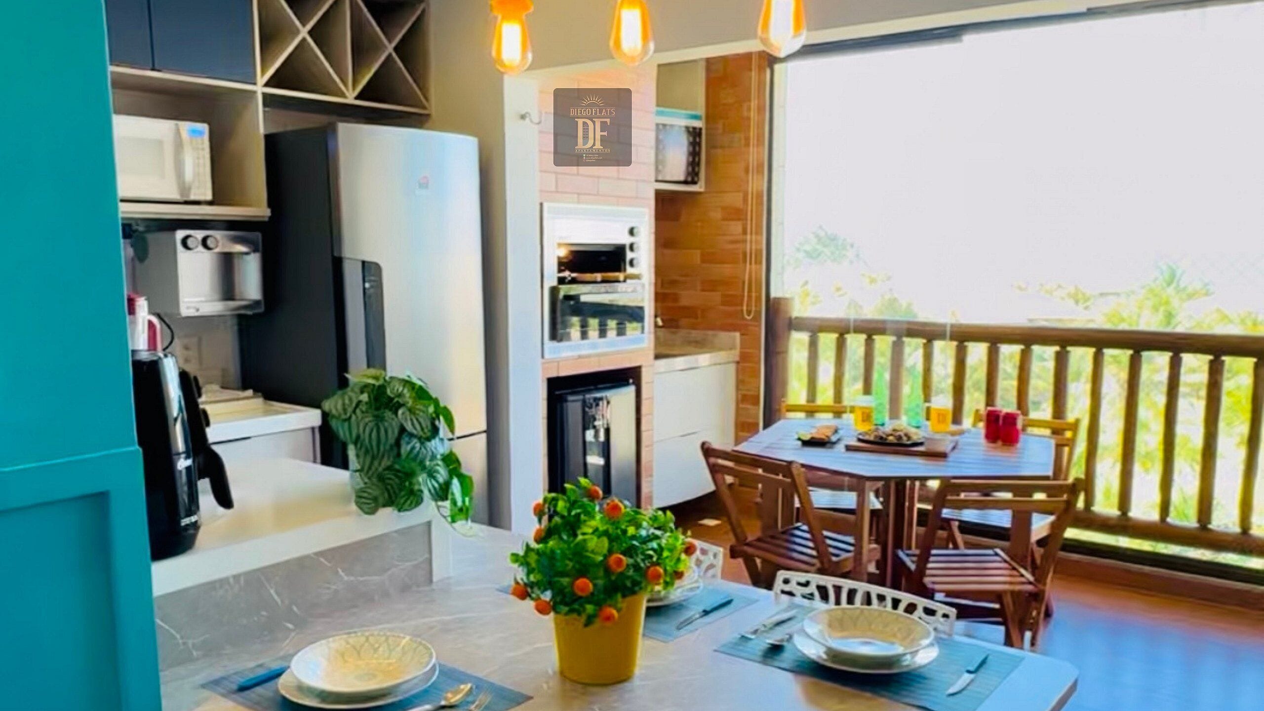 Una cocina equipada con microondas, horno y refrigerador, una mesa de comedor con sillas, y un balcón con barandilla.