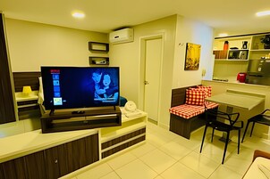 Quarto de hotel pequeno com televisão, sofá, mesa de jantar e área de cozinha.