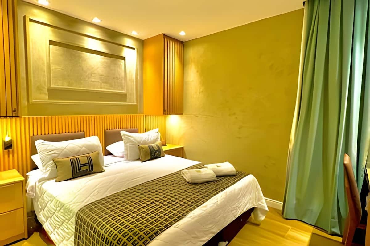 Une chambre d’hôtel avec un lit, une table de chevet, une lampe fixée au mur et un rideau.