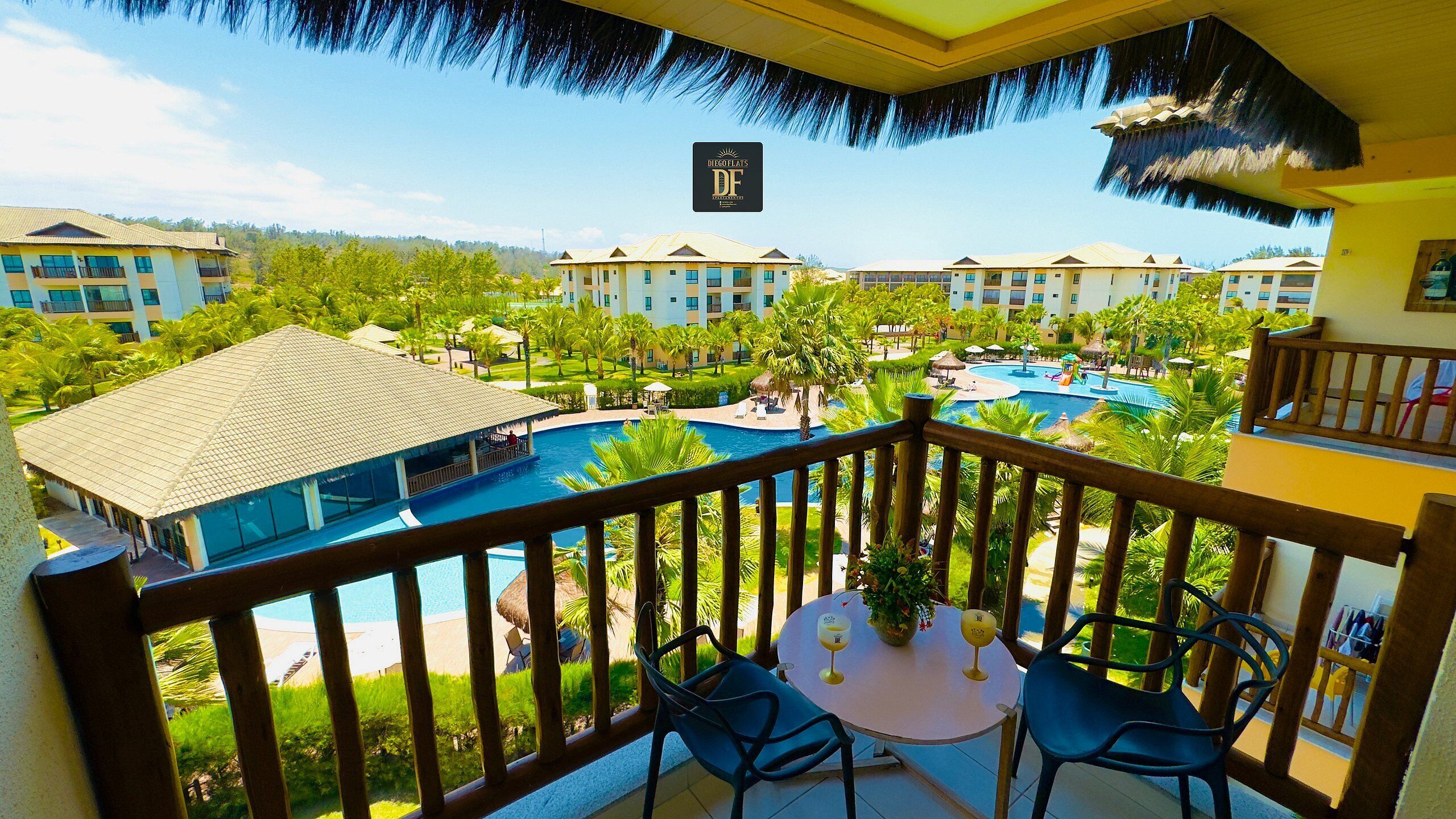 A hotel balcony with a pool view, a table with two chairs, and a sign with 'DF' logo.