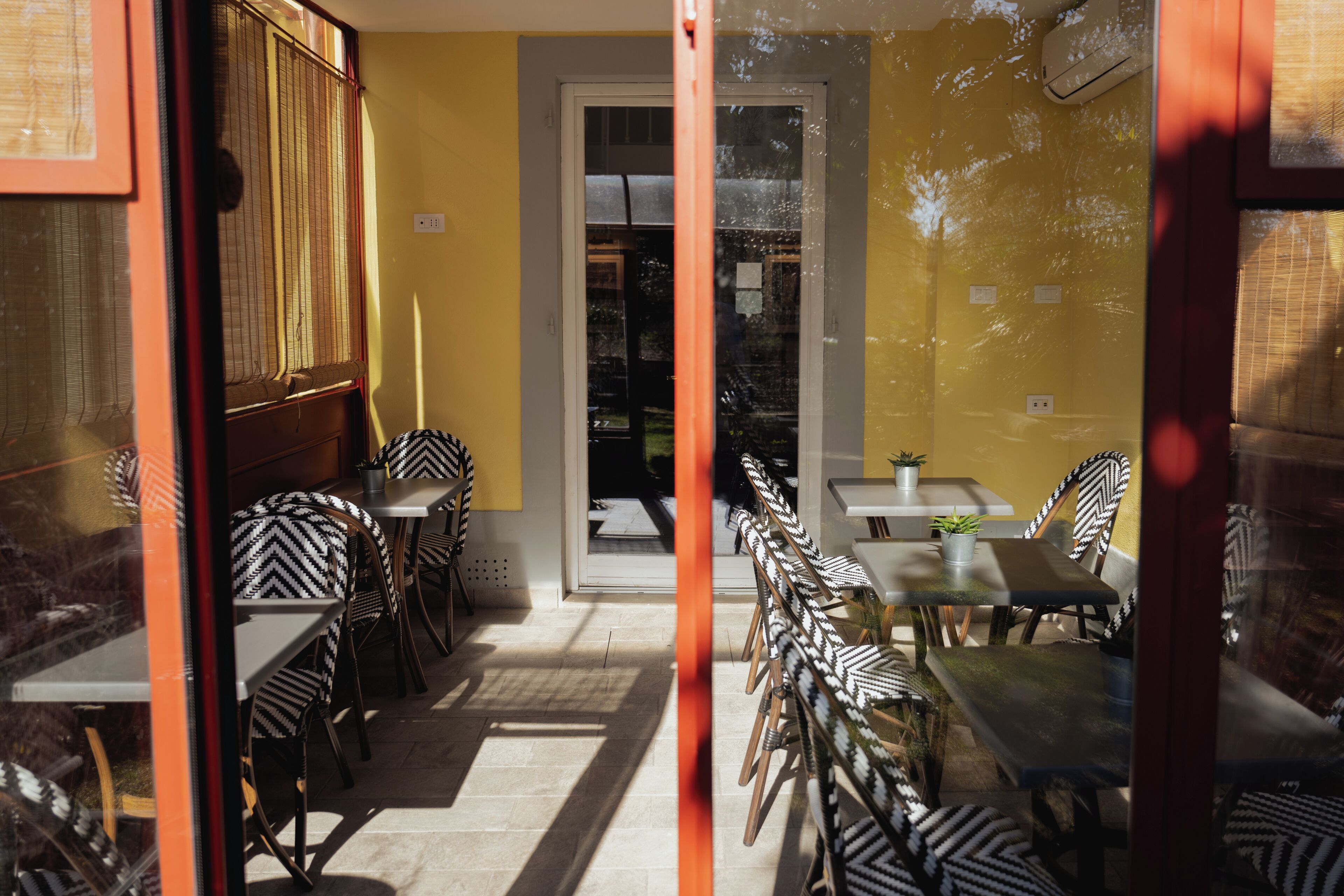 An indoor seating area with tables and chairs, a door leading outside, and a yellow wall.