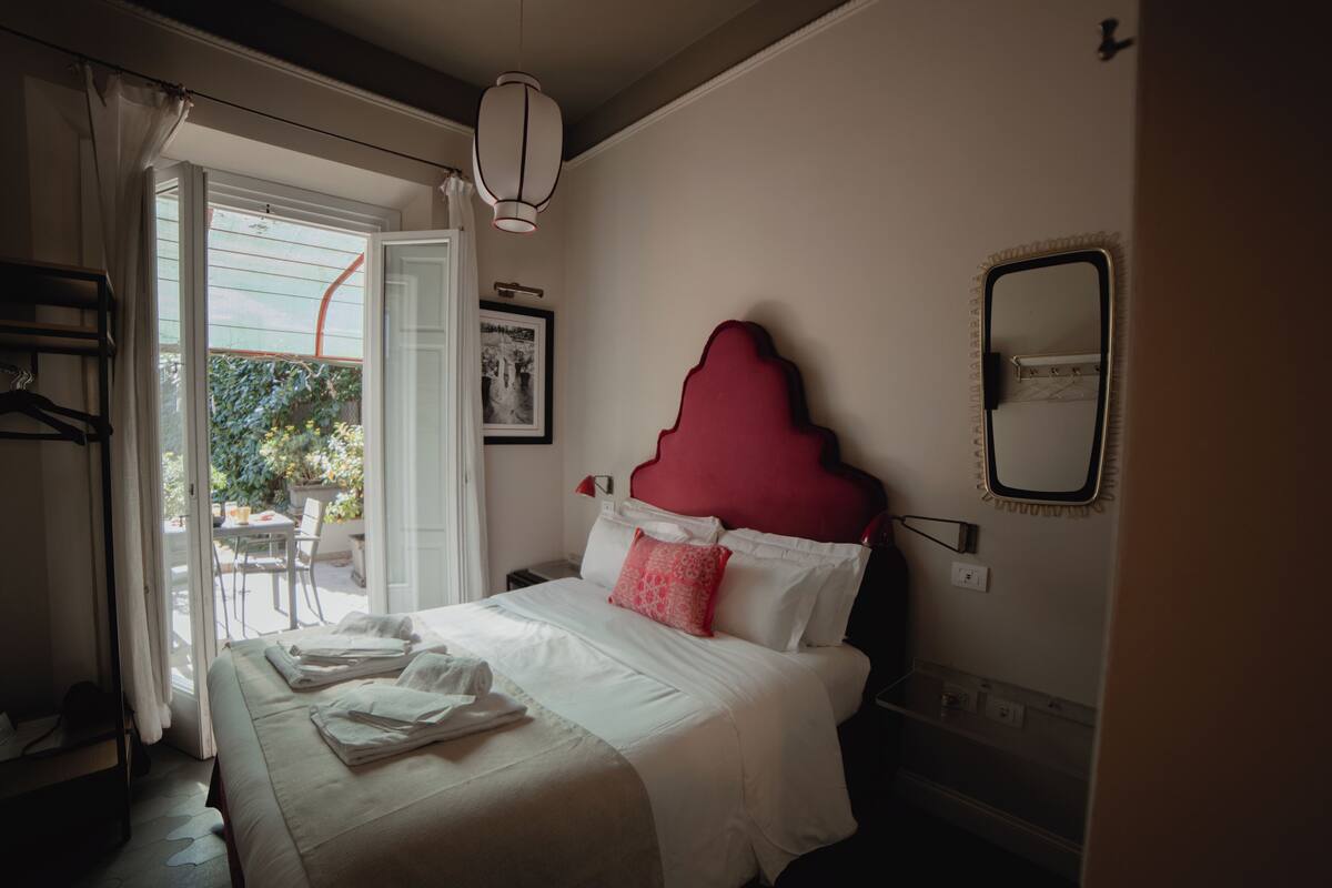 A hotel room with a bed, a bedside table, a mirror, and a window with curtains.