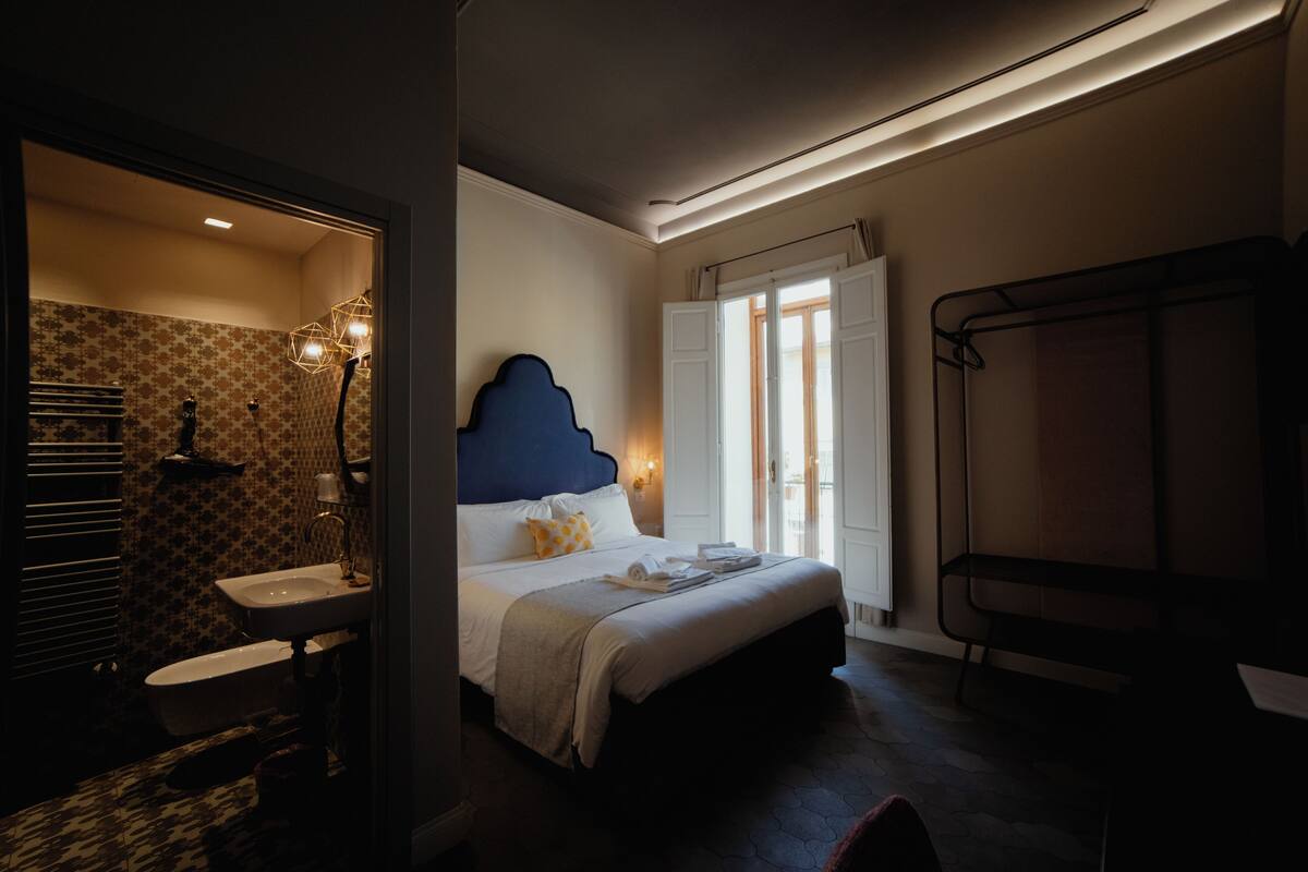 A hotel room with a bed, a bathroom with a sink, and a window with curtains.