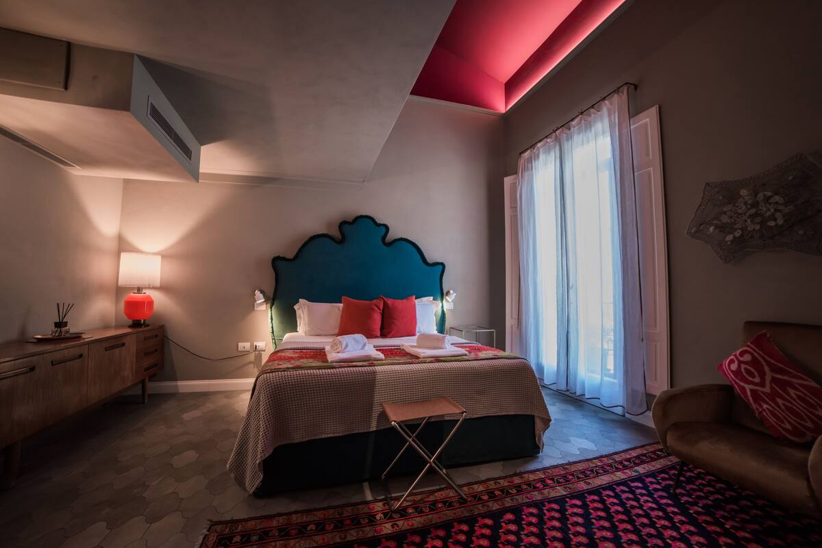 A bedroom with a bed, bedside table, lamp, and a window with curtains.