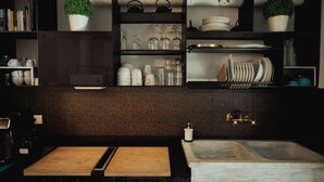Una cocina moderna con encimera de madera, un fregadero y repisas superiores con cristalería, platos y plantas en macetas.
