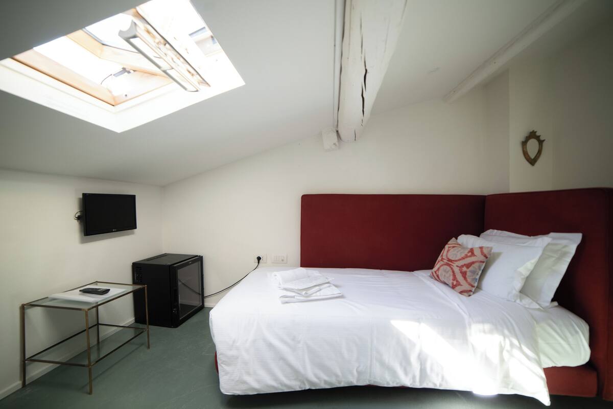 A bedroom with a bed, a TV mounted on the wall, a small table, and a ceiling light fixture.
