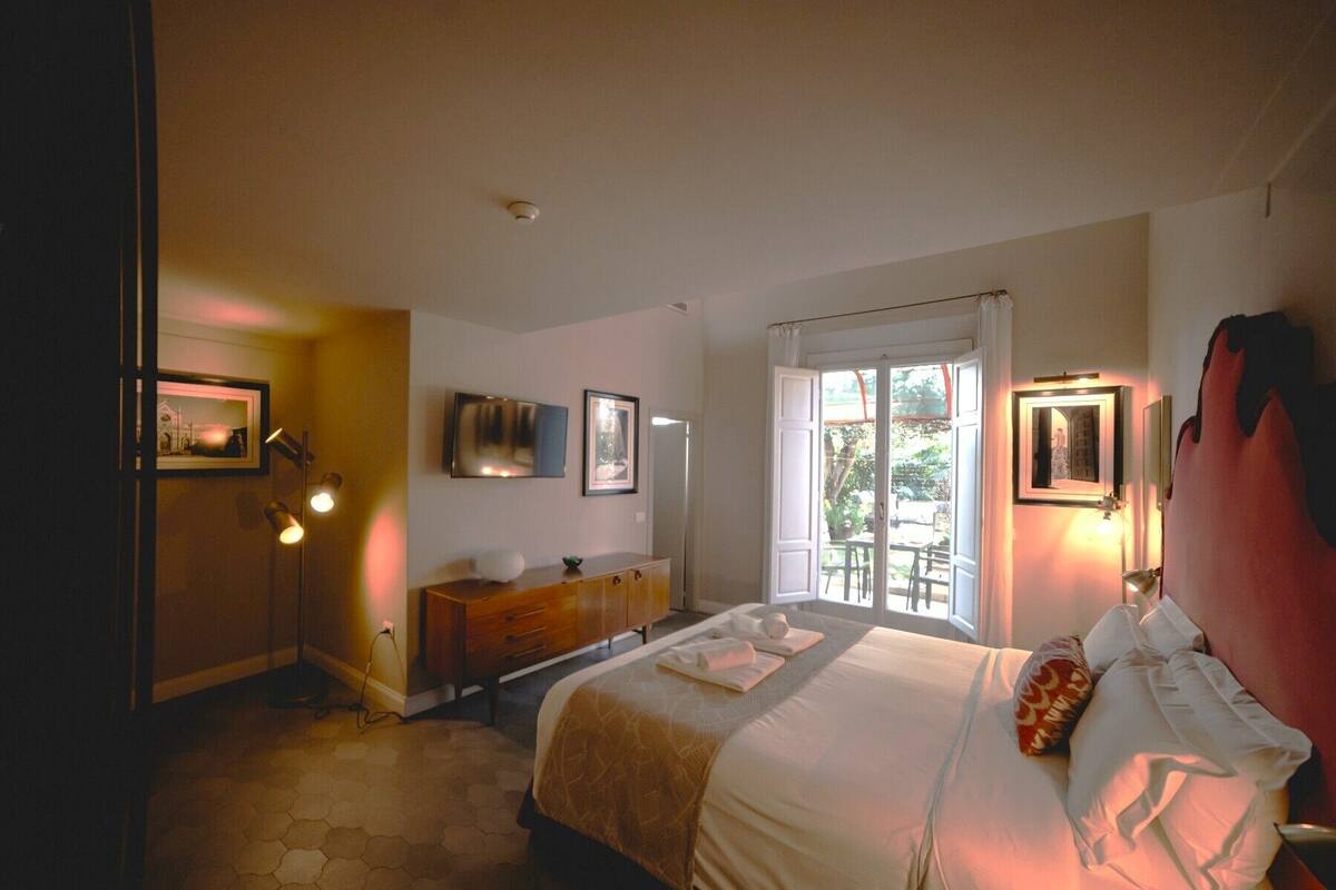 A hotel room with a bed, bedside tables, a TV, and a window with a view of the outdoors.