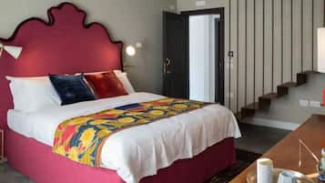 Habitación de hotel con una cama grande, cabecera roja, escritorio de madera y una escalera al fondo.