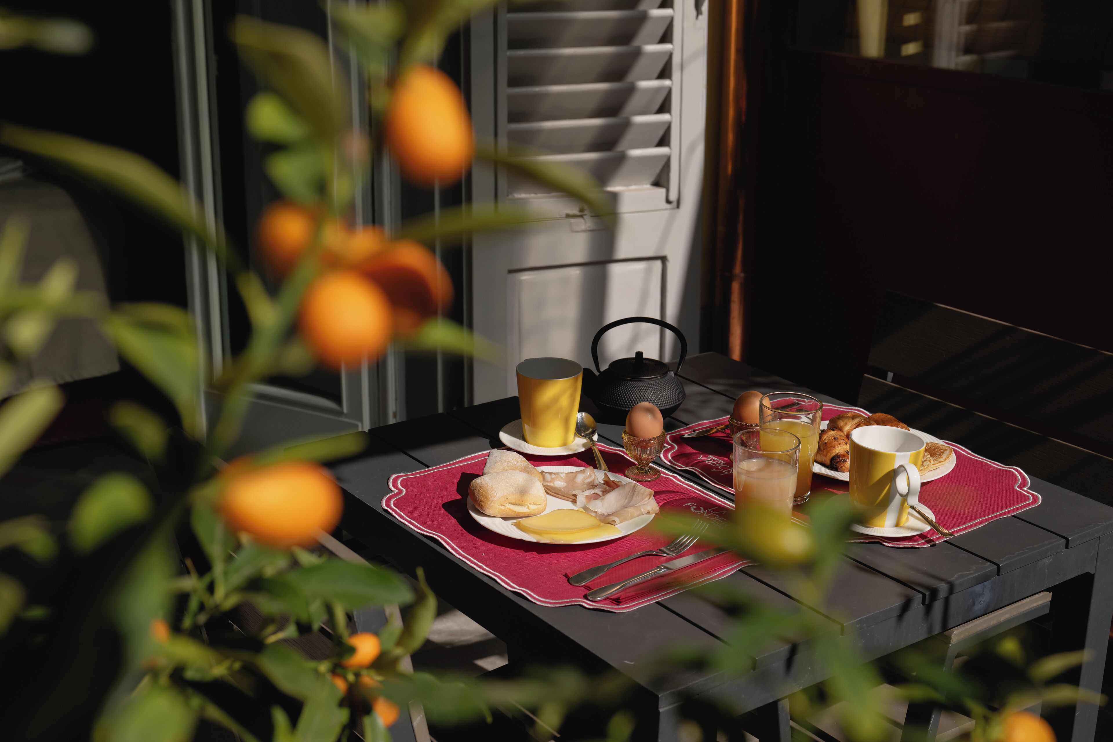 Taula preparada amb articles per esmorzar, com ara ous, torrades i suc, amb vista a una finestra i una planta amb fruits taronja.
