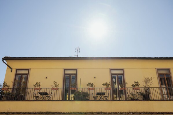A building with a yellow facade, a balcony with a black railing, and a satellite dish on the roof.