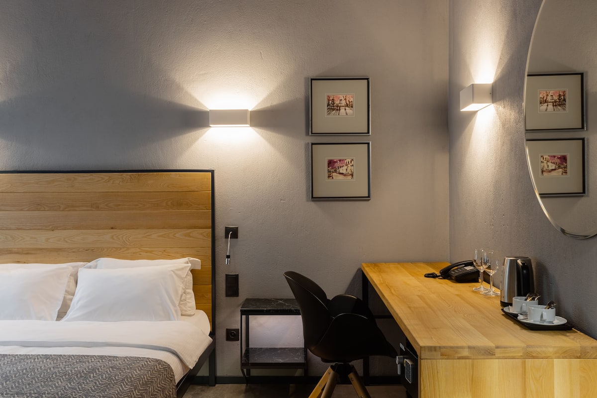 A hotel room with a bed, a desk with a telephone, a coffee maker, and two framed pictures on the wall.