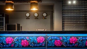 Zona d'entrada d'un hotel amb tres rellotges a la paret, una catifa estampada amb motius florals i un espai d'espera amb una banca.