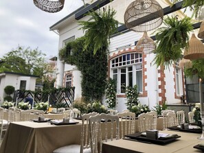 An outdoor dining area with white chairs and tables, surrounded by greenery and decorative hanging lamps. - Serguzest Otel (Adalar)