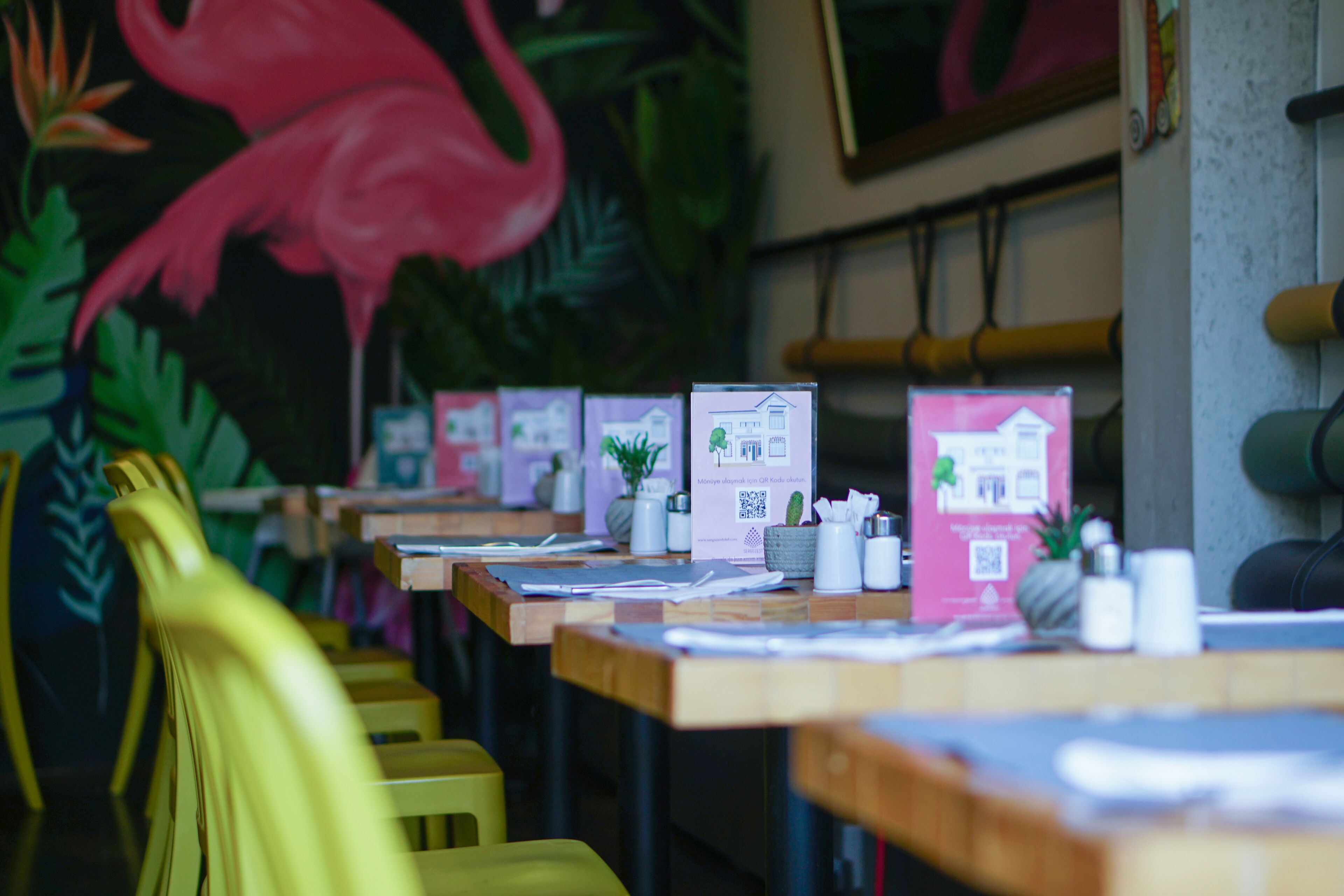Un interior de restaurante con mesas y sillas de madera, y un mural de un flamenco.