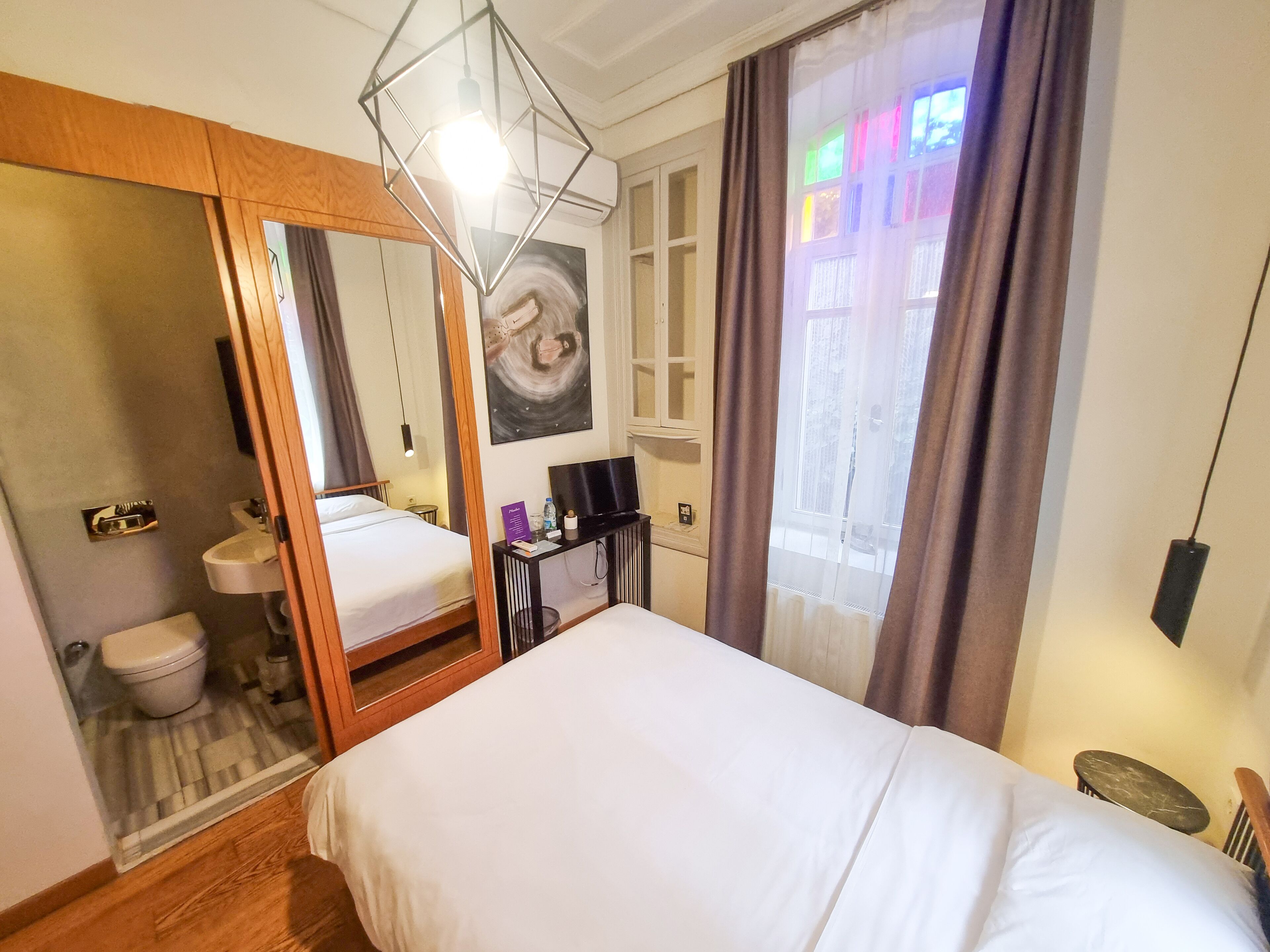 A hotel room with a bed, a bathroom, a desk with a TV, and a window with curtains.