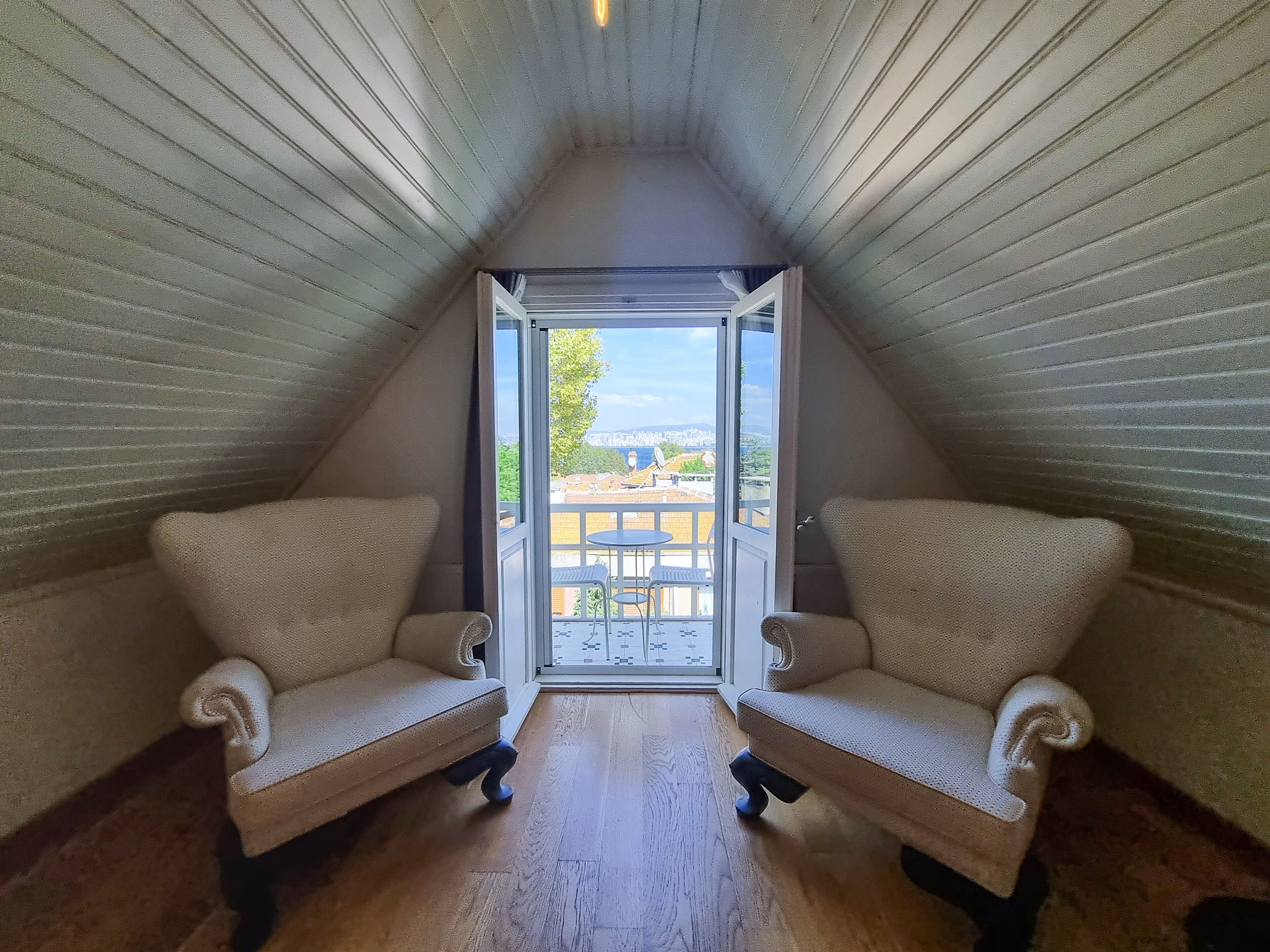 A room with a sloped ceiling and two armchairs facing a balcony with a view of a cityscape.