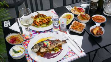 A table set with various dishes, including a whole fish, bowls of dips, and a bottle of wine.