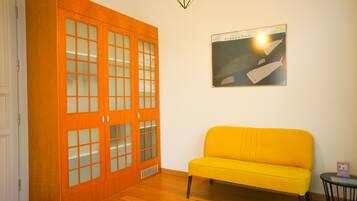 A room with a wooden wardrobe, a yellow sofa, and a framed picture on the wall.