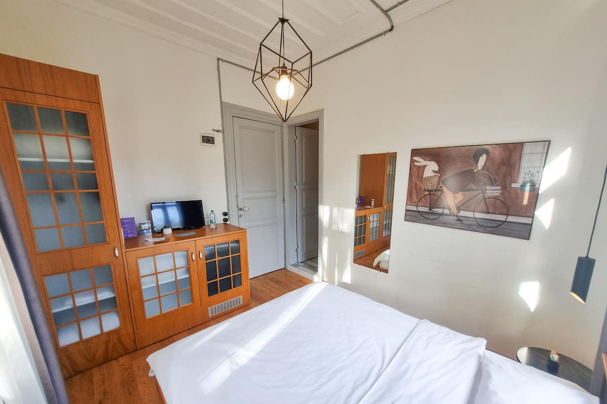 A bedroom with a bed, a wooden cabinet with a television, and a door leading to another room.
