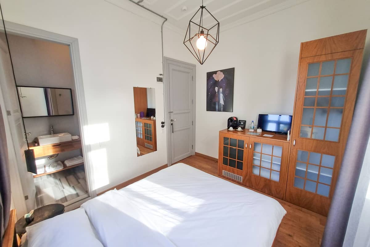 A bedroom with a bed, a wooden wardrobe, a television, and a bathroom with a mirror and sink.