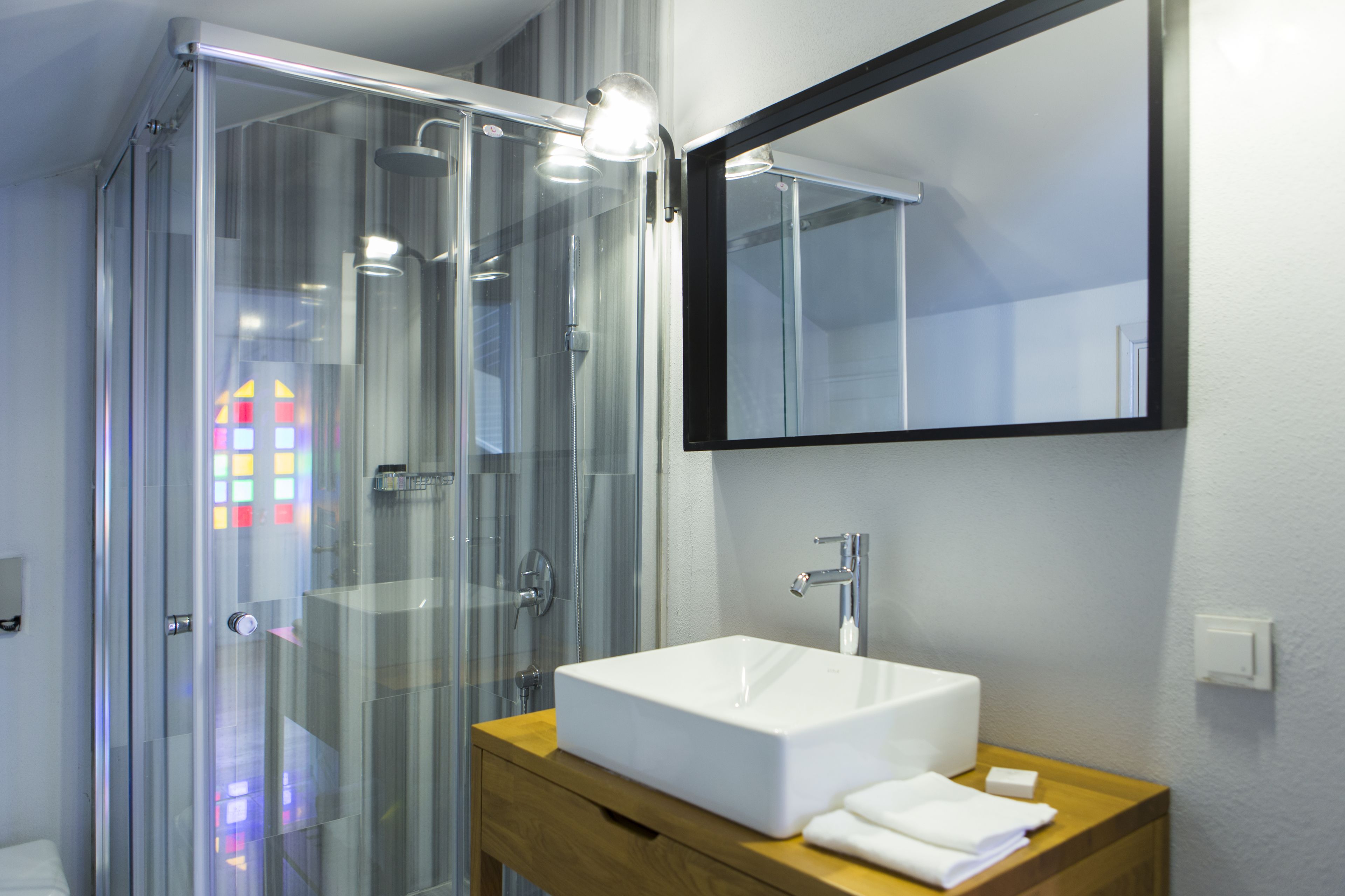 A modern bathroom with a glass shower enclosure, a white sink, and a mirror.