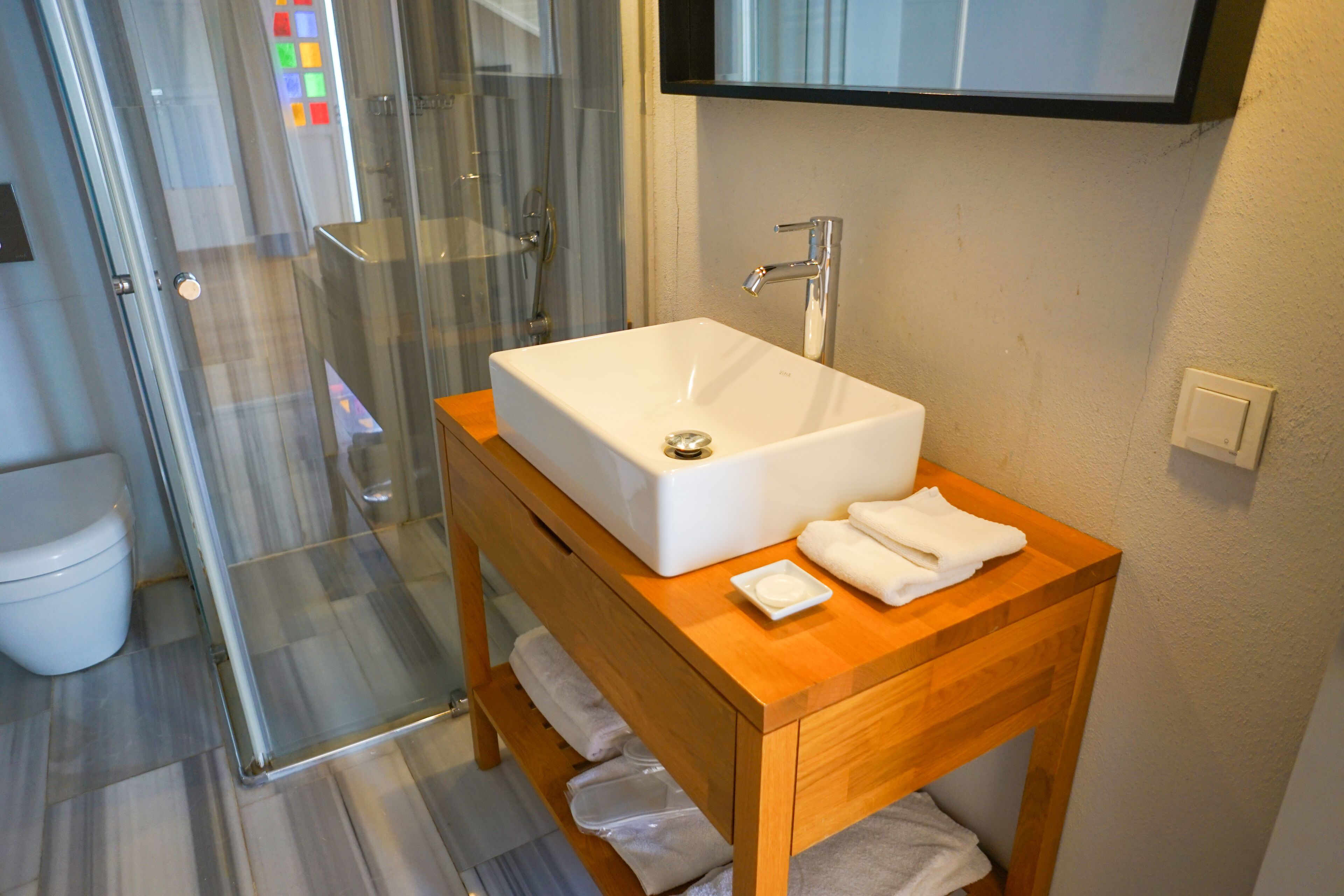 A bathroom with a glass shower enclosure, a white sink on a wooden vanity, and a toilet.