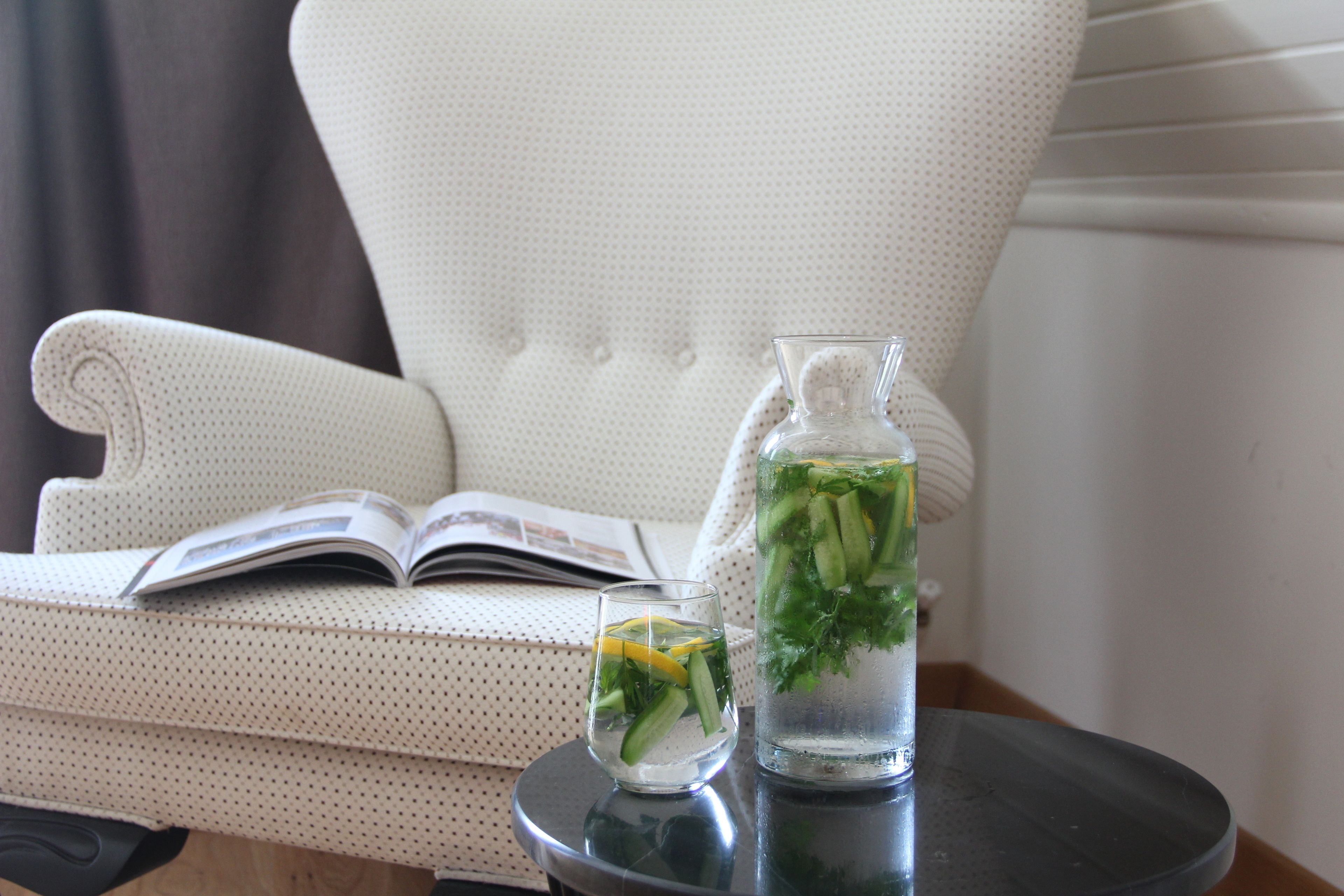 Une pièce avec un canapé blanc recouvert de tissu, une petite table ronde sur laquelle se trouvent une carafe d’eau et un verre, et un livre ouvert posé sur le canapé.