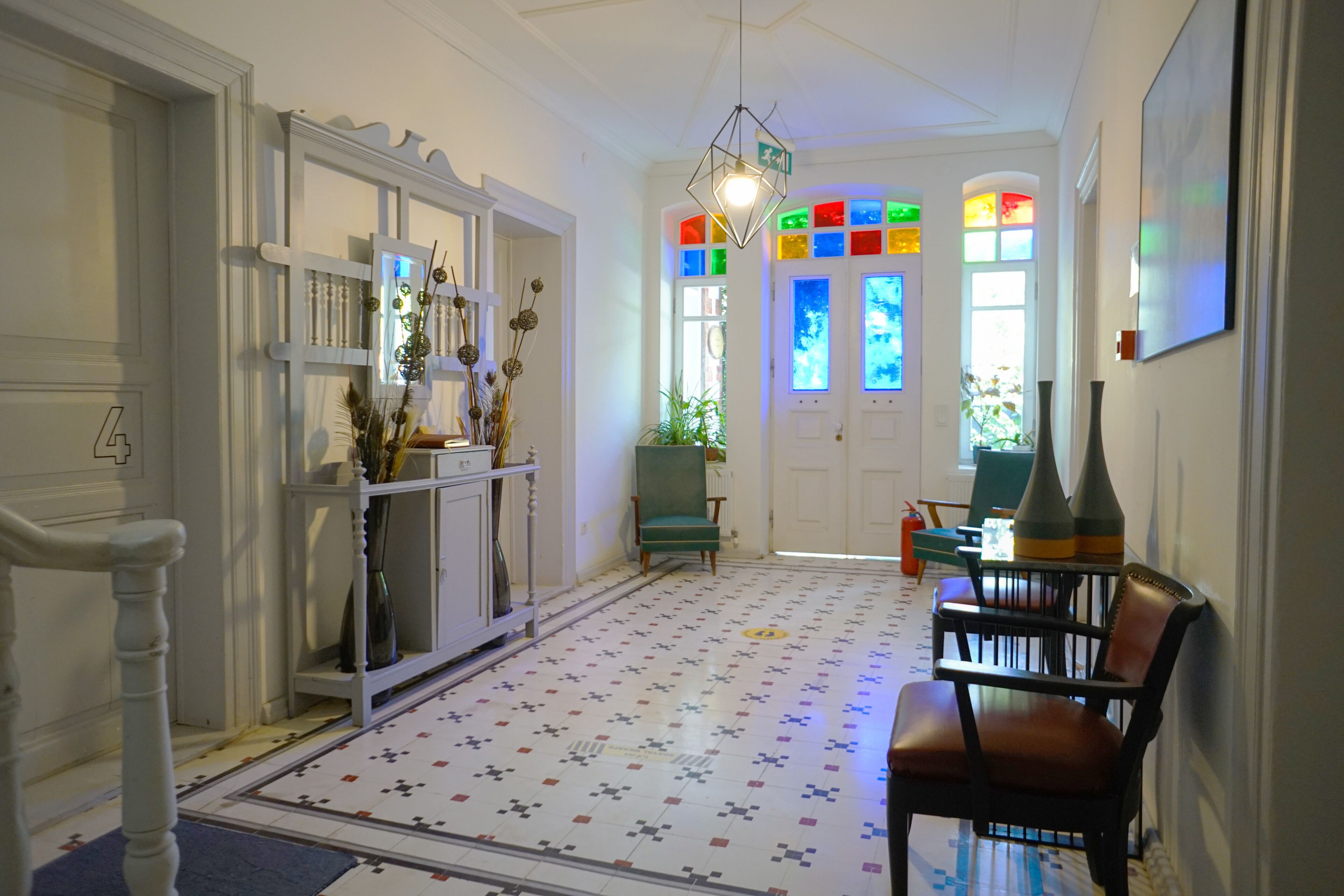 A hallway with patterned flooring, a green chair, and a table with a vase.