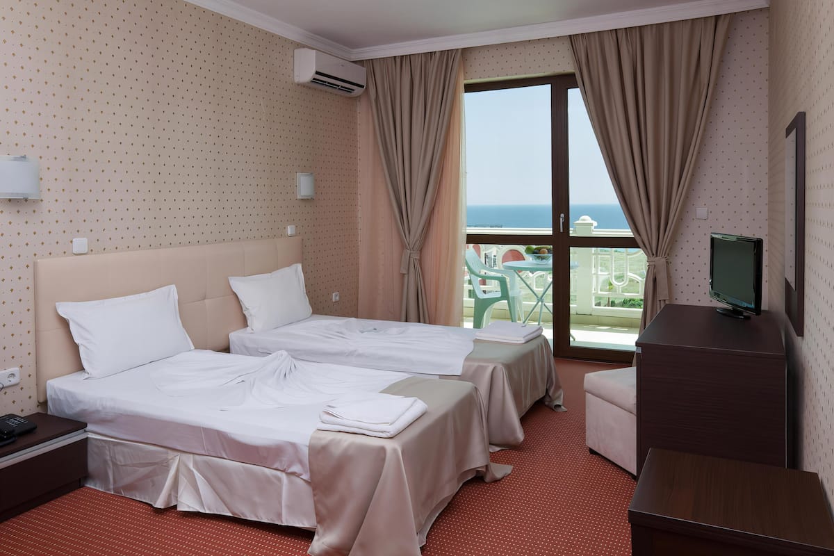 A hotel room with two beds, a TV, and a balcony with a view.
